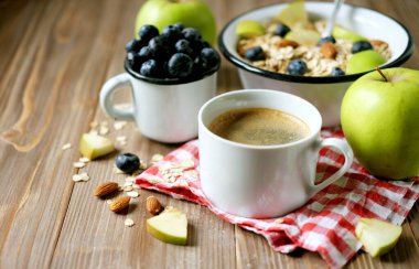 Tahta bir masada yulaf lapası, kahve, elma, böğürtlen ve fındık..