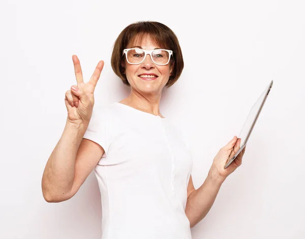 Portrait of attractive trendy cheerful elderly woman using tablet pointing up