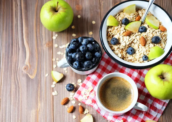 Oatmeal porridge, coffee, apple, berries and nuts on a wooden table. — Stock Photo, Image