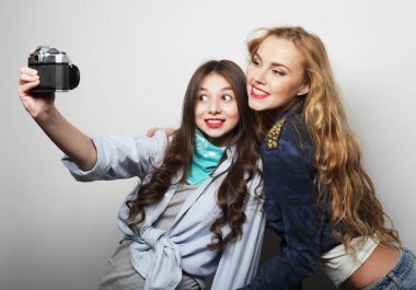 Mutlu genç bayan arkadaşlar, gri arka planda fotoğraf çekiyorlar.