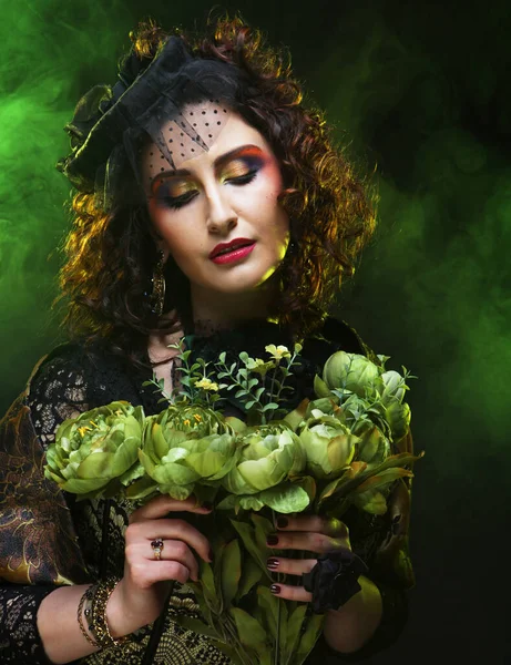 Parlak, yaratıcı makyajlı ve elinde kuru çiçekler tutan yeşil peruklu genç bir kadın. — Stok fotoğraf