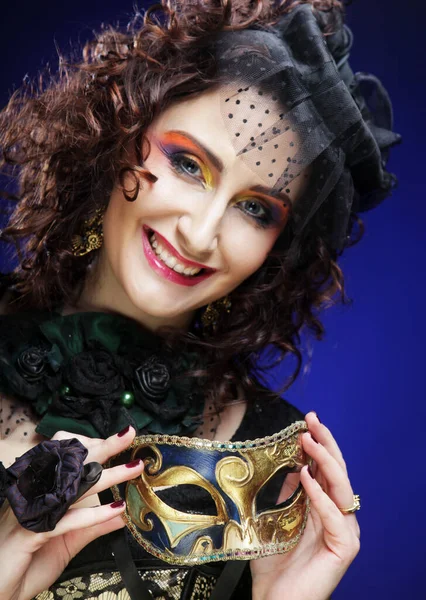 Όμορφη νεαρή γυναίκα με φωτεινό μακιγιάζ και καπέλο με πέπλο κρατώντας βενετσιάνικη μάσκα — Φωτογραφία Αρχείου