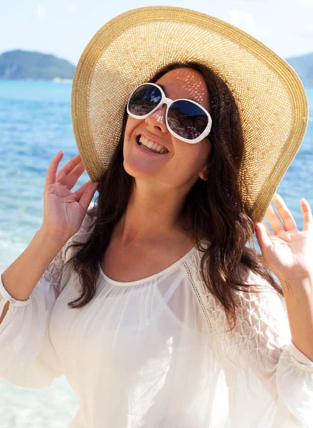 Happy woman wearing summer white dress, hat and sunglasses on beach.