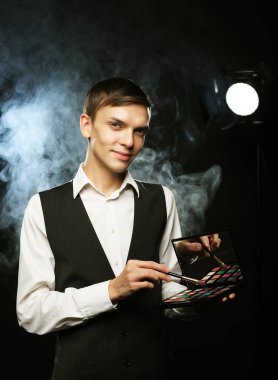 Profesyonel makyaj sanatçısı Studio, poz gölgeler paleti tutar. Duman arka planı. Genç Moda adam. yakın çekim