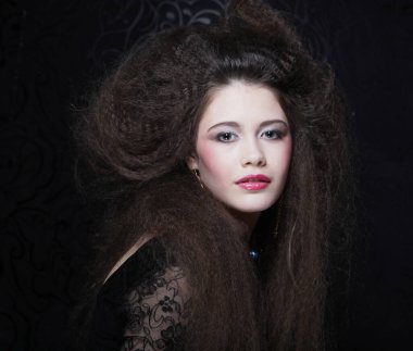 Uzun kıvırcık saçlı, akşam makyajlı, siyah elbiseli ve mücevher takan güzel bir kadın.