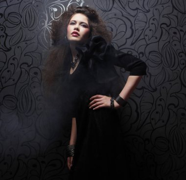 Uzun kıvırcık saçlı, akşam makyajlı, siyah elbiseli ve mücevher takan güzel bir kadın.