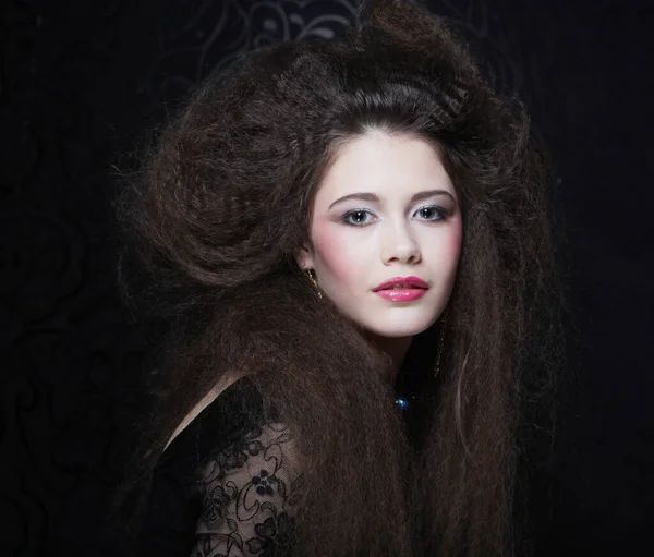 Uzun kıvırcık saçlı, akşam makyajlı, siyah elbiseli ve mücevher takan güzel bir kadın.