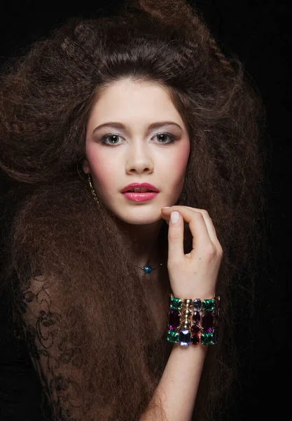 Uzun kıvırcık saçlı, akşam makyajlı, siyah elbiseli ve mücevher takan güzel bir kadın.