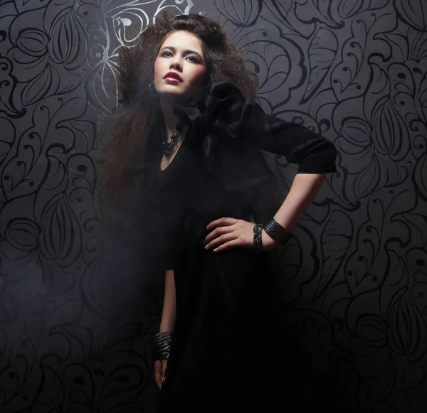 Uzun kıvırcık saçlı, akşam makyajlı, siyah elbiseli ve mücevher takan güzel bir kadın.