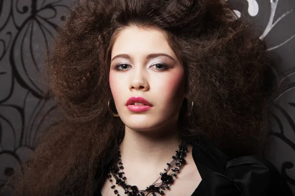 Uzun kıvırcık saçlı, akşam makyajlı, siyah elbiseli ve mücevher takan güzel bir kadın.