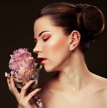 Zarif renklerde makyajlı güzel bir kadın büyük pembe bir çiçek tutuyor, güzellik konsepti.