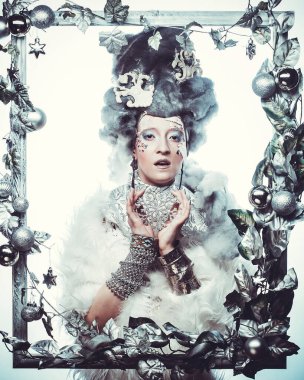 Parti, Noel ve insanlar: Noel karnavalı için kostüm giymiş güzel bir kadın Noel süslemeleri ve gümüş yapraklar çerçevesinde poz veriyor. Yaratıcı makyaj, saç stili.