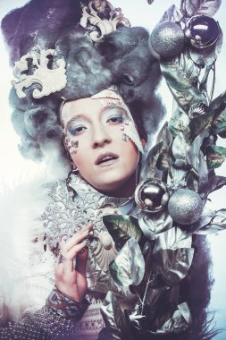 Parti, Noel ve insanlar: Noel karnavalı için kostüm giymiş güzel bir kadın Noel süslemeleri ve gümüş yapraklar çerçevesinde poz veriyor. Yaratıcı makyaj, saç stili.