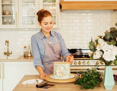 Yaşam tarzı, yemek pişirme ve serbest çalışma konsepti: Güzel genç bir kadın pastayı boyayla süslüyor. Bir yemek blogcusu yeni bir tarif keşfediyor. Ev işleri ve yeni fırsatlar.
