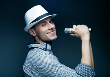 Gri arkaplanda mikrofona şarkı söyleyen şapkalı yakışıklı bir genç resmi. Yaşam tarzı ve insan kavramı.