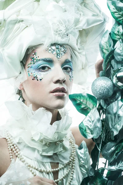 Parti, Noel ve insanlar: Noel karnavalı için kostüm giymiş güzel bir kadın Noel süslemeleri ve gümüş yapraklar çerçevesinde poz veriyor. Yaratıcı makyaj, saç stili.