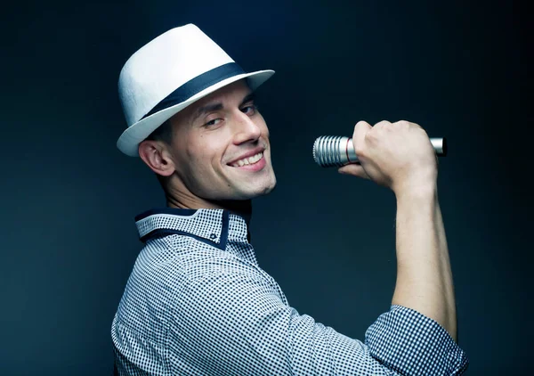 Gri arkaplanda mikrofona şarkı söyleyen şapkalı yakışıklı bir genç resmi. Yaşam tarzı ve insan kavramı.