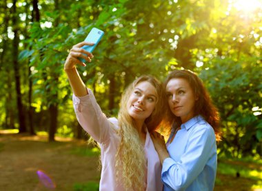 Yaşam tarzı, duygu, aile ve insan kavramı: olgun anne ve yetişkin kız yaz parkında cep telefonuyla selfie çekiyor