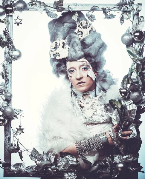 Parti, Noel ve halk konsepti: Gümüş sanatsal makyajlı, peruklu, Noel süslemeleri ile süslenmiş gümüş çerçevede poz veren yaratıcı görünümlü genç kadın. Kış Portresi. Kar Kraliçesi.