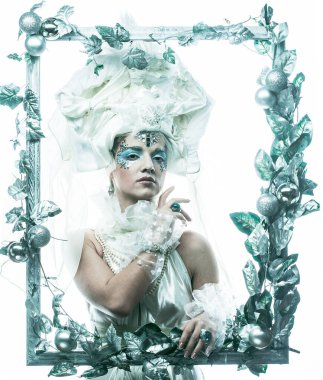 Parti, Noel ve insanlar: Noel karnavalı için kostüm giymiş güzel bir kadın Noel süslemeleri ve gümüş yapraklar çerçevesinde poz veriyor. Yaratıcı makyaj, saç stili.