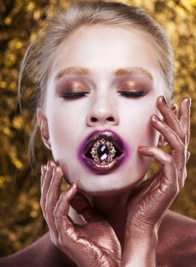 Ağzında değerli bir yüzük tutan çekici genç bir manken. Parlak makyaj, dudaklarında altın..