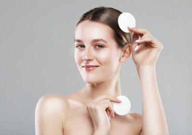 Makyaj malzemelerini çıkarmak için pamuk pedleri tutan güzel bir kadın. Temizlik, günlük rutin işler. Gri arkaplanda bir portre.