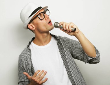 Karaoke zamanı. Şapkalı genç adam beyaz arka planda mikrofonla şarkı söylüyor..