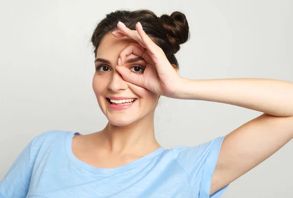 Vrolijke vrolijke vrouw kijkt door nul of ok gebaar, houdt afgeronde vingers in de buurt van oog — Stockfoto