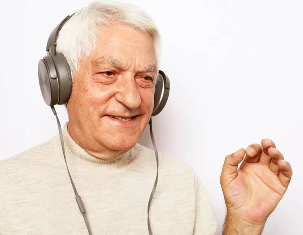 Lifestyle, tehnology and old people concept: image of an elderly gray-haired man listening to music with headphones — Stock Photo, Image