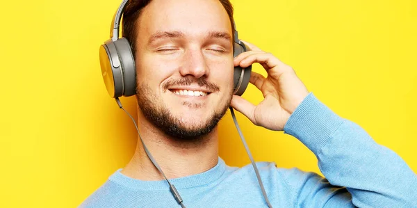 Životní styl a lidé koncept: mladý muž nosí sluchátka a drží mobilní telefon přes žluté pozadí. — Stock fotografie