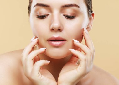 Temiz tenli güzel genç bir kadın bej arka planda yüzüne dokunuyor. Kozmetik, güzellik ve kaplıca konsepti.