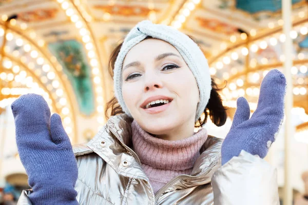 Pretty woman in winter clothes posing against the backdrop of a carousel at the Christmas market, winter portrait.