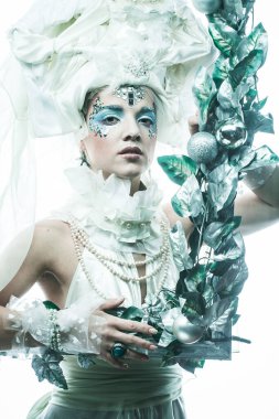 Parti, Noel ve insanlar: Noel karnavalı için kostüm giymiş güzel bir kadın Noel süslemeleri ve gümüş yapraklar çerçevesinde poz veriyor. Yaratıcı makyaj, saç stili.