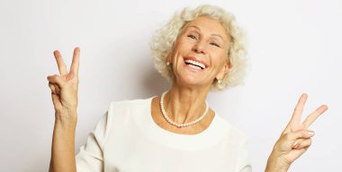 Sevimli, buruşuk, buruşuk bir kadın gülümseyerek barış işareti yapar, serin ve güzel bir günün tadını çıkarır..