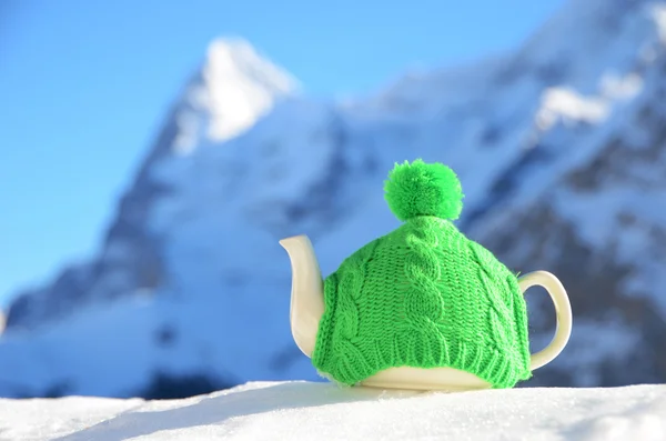 Tea pot in the knitted cap on the snow — Stock Photo, Image