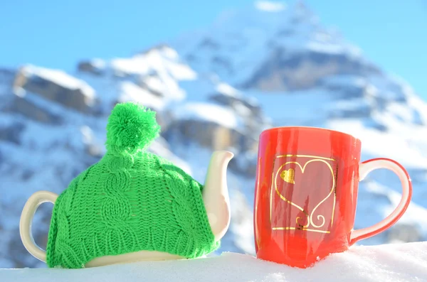 Tea pot in the cap and a cup against alpine scenery — Stock Photo, Image