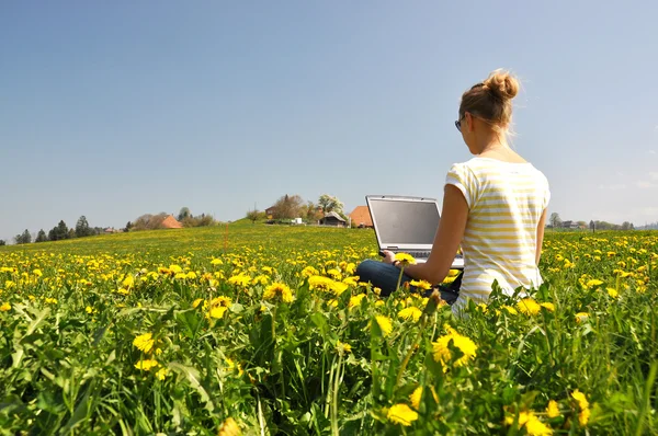 Ragazza con un computer portatile sul prato primaverile — Foto Stock