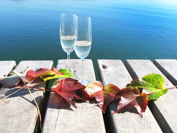 Dos winglasses y hojas de otoño en un embarcadero de madera — Foto de Stock