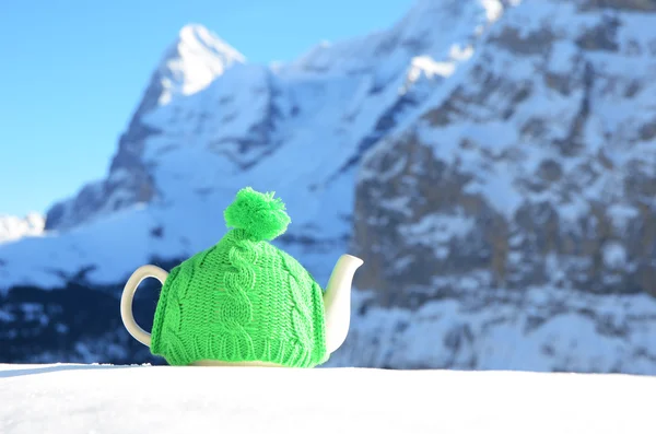 Tea pot in the knitted cap on the snow against mountain peak — Stock Photo, Image