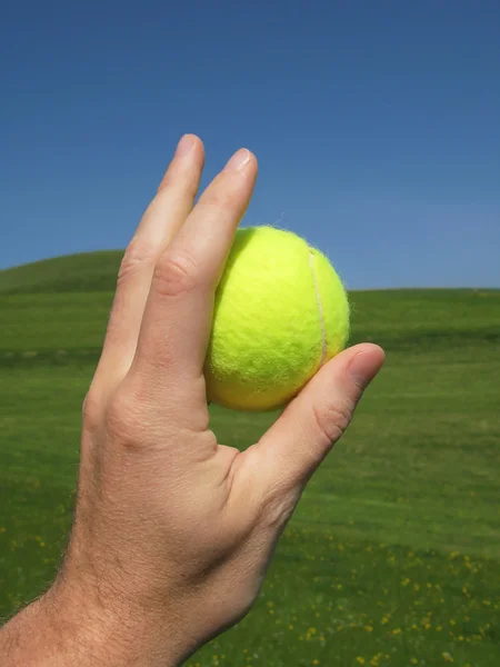 Tennis ball in the hand against scenic hills — Stock Photo, Image