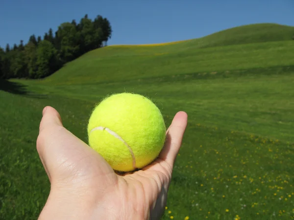 Tennis ball in the hand against scenic hills — Stock Photo, Image