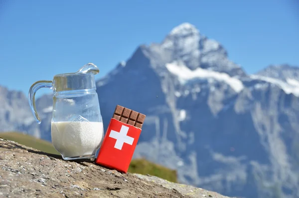 Swiss chocolate and jug of milk against mountain peak. Switzerla — Stock Photo, Image