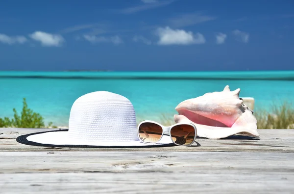 Gafas de sol, sombrero y caracol contra el océano. Exuma, Bahamas —  Fotos de Stock