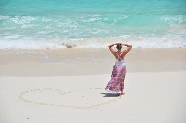 Menina desenhando um coração na praia arenosa — Fotografia de Stock