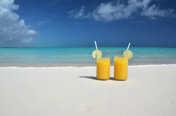 Dos vasos de jugo de naranja en la playa de arena —  Fotos de Stock