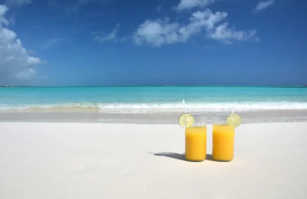 Dos vasos de jugo de naranja en la playa de arena —  Fotos de Stock