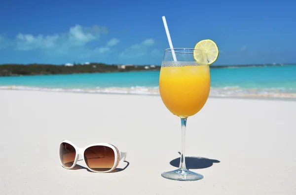 Jugo de naranja y gafas de sol en la playa . — Foto de Stock