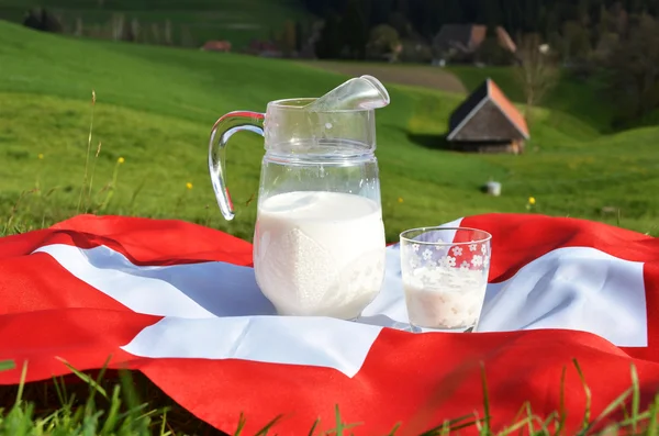 Kruik van melk op de Zwitserse vlag. — Stockfoto