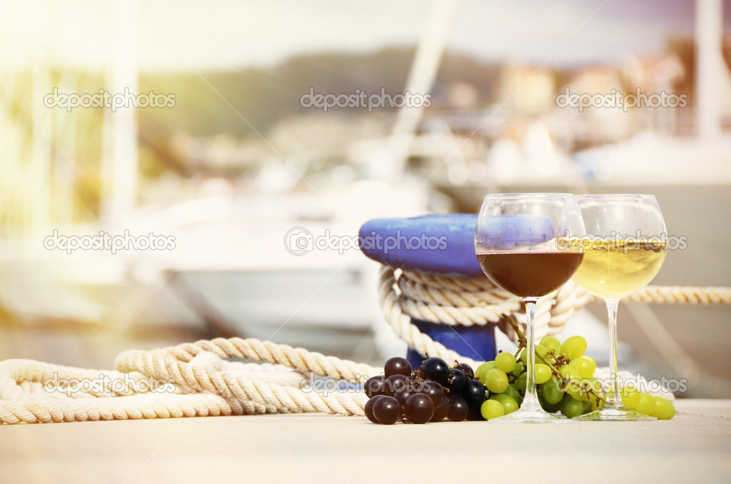 Pair of wineglasses and grapes against the yacht pier