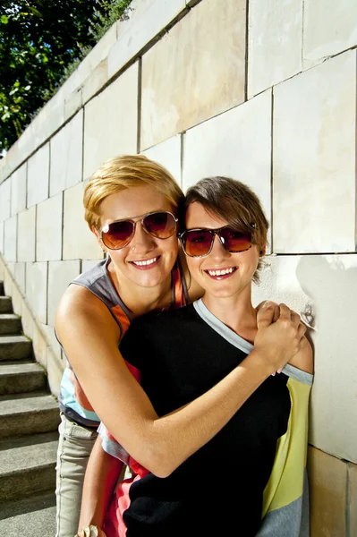 Две красивые женщины в солнечных очках на фоне каменной стены — стоковое фото